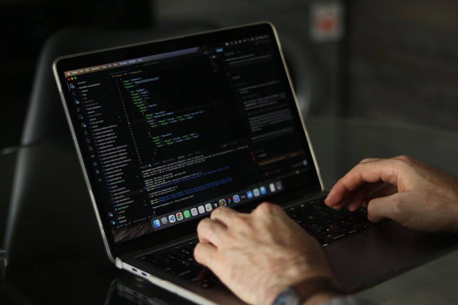 A close-up view of a person working outdoors with a computer, featuring a large monitor displaying lines of code. The background shows a garden with well-maintained grass, flower beds edged with neat 